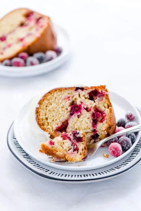 a slice of gluten free cranberry orange bundt cake on a small white plate with a small bite of cake on a fork
