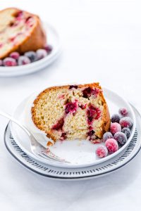 a piece of gluten free cranberry orange bundt cake on a small white plate with a bite taken out