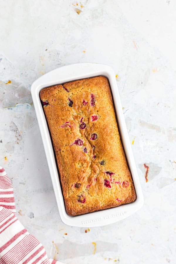 a baked loaf of gluten free white chocolate cranberry bread in a white loaf pan