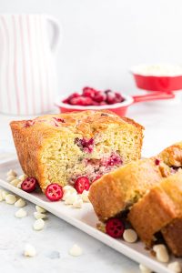 a loaf of gluten free white chocolate cranberry bread on a white plate that's been sliced into