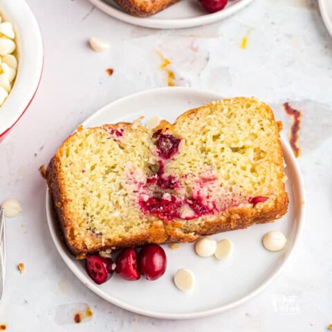 sliced gluten free white chocolate cranberry bread on a white plate garnished with fresh cranberries and white chocolate chips