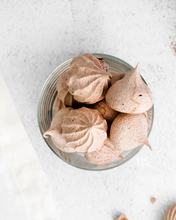 overheard shot of dark chocolate meringue cookies in a round glass cup