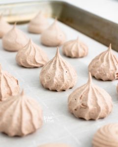 baked dark chocolate meringue cookies on a parchment lined sheet pan