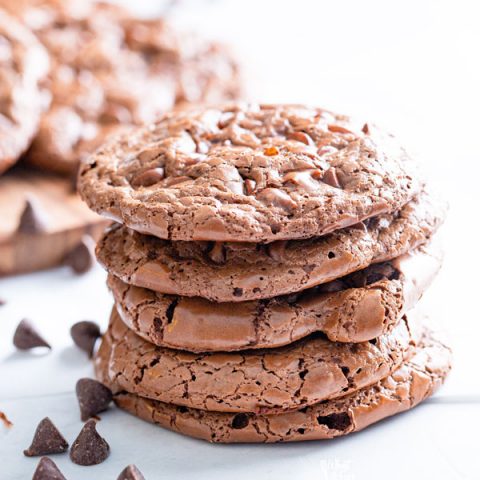 A stack of 5 flourless chocolate cookies garnished with chocolate chips scattered around