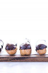 gluten free chocolate eclairs lined up on a wood board lined with wax paper