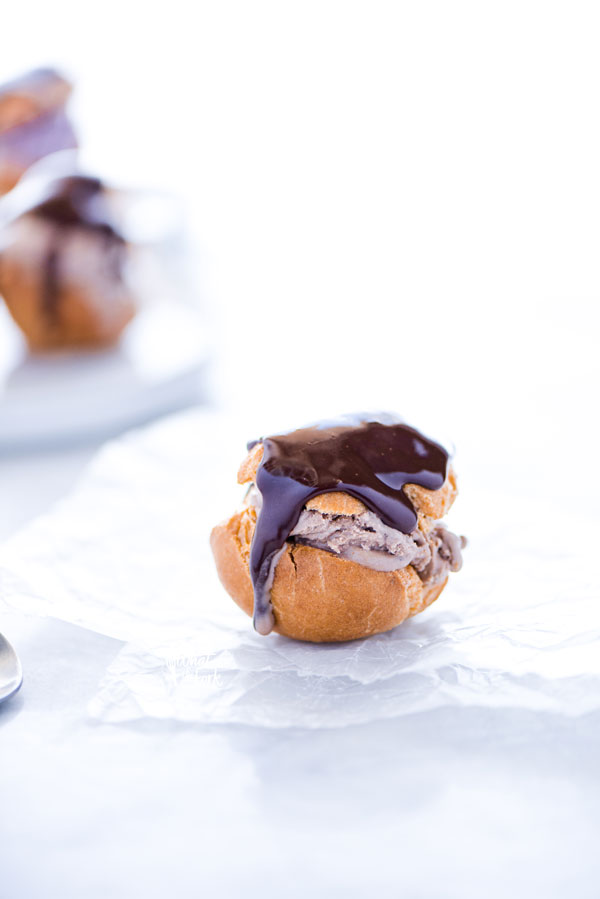 a single gluten free Choux Pastry shell filled with chocolate ice cream and topped with chocolate ganache on top of wax paper