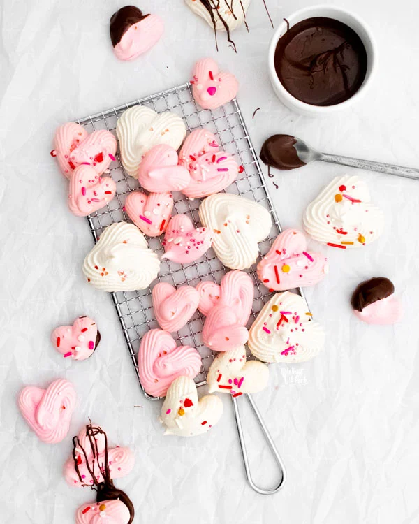 heart meringue cookies on and scattered around a small wire rack ready to be drizzled with melted chocolate