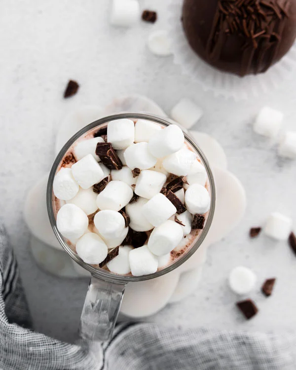 overhead shot of hot cocoa topped with chocolate and marshmallows in a clear glass mug