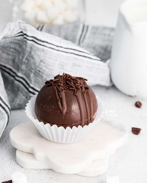 A homemade hot chocolate balls in a white paper liner on top of two white marble coaster