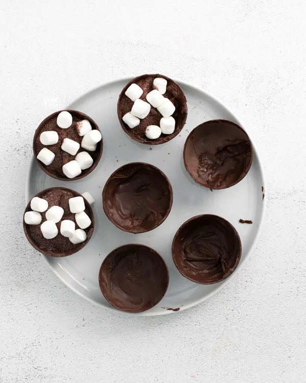overhead shot of hot chocolate bombs being filled on a white plate