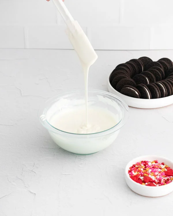 white chocolate being drizzled from a spatula into a bowl of melted white chocolate