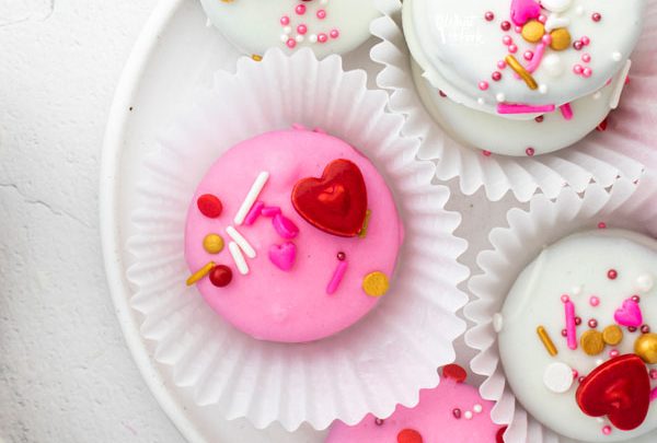 overhead shot of pink and white Valentine's Chocolate Covered Oreos in white paper holders on a white plate