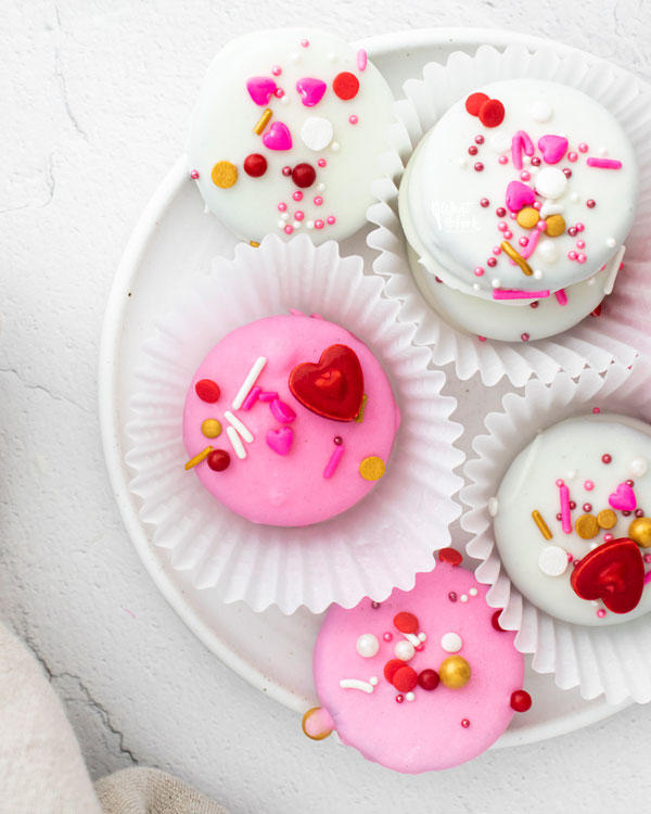 overhead shot of pink and white Valentine's Chocolate Covered Oreos in white paper holders on a white plate