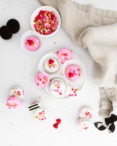 overheard shot of Valentine's Chocolate Covered Oreos on a white plate and scattered on a white surface