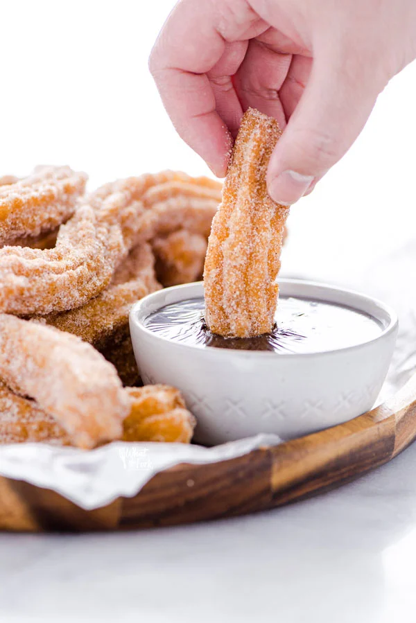 a gluten free churros being dipped into chocolate sauce