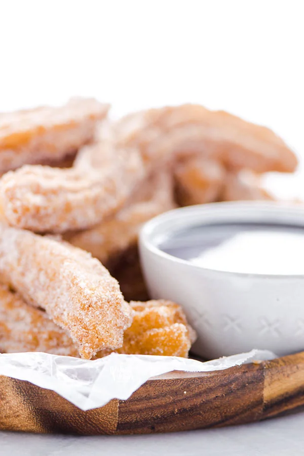 close up of gluten free churros on a wood platter lined with wax paper