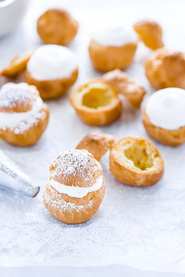 gluten free cream puffs on wax paper being filled with whipped cream