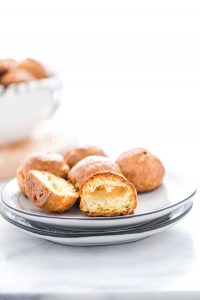 gluten free Gougères on a stack of white plates with one cut in half to show the inside