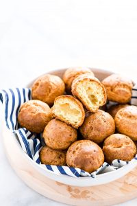 gluten free Gougères in a napkin lined bowl with one cut in half to show the inside