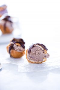 a gluten free profiterole filled with chocolate ice cream and topped with chocolate ganache that's been cut in half to show the center