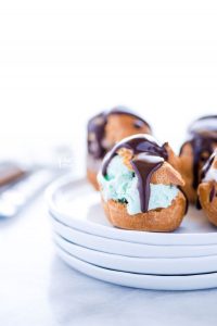 a gluten free profiterole filled with mint chocolate chip ice cream and topped with chocolate ganache on a stack of white plates