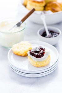 a gluten free scone on a stack of white plates that's been split in half and topped with clotted cream and jam