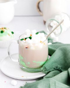 hot cocoa in a clear glass mug made with a St. Patrick's Day hot chocolate bomb