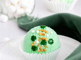 a green St. Patrick's Day Hot Cocoa Bombs in a white paper liner on a white plate
