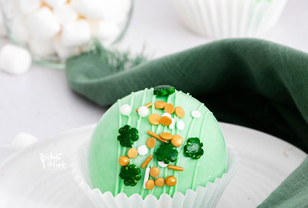 a green St. Patrick's Day Hot Cocoa Bombs in a white paper liner on a white plate