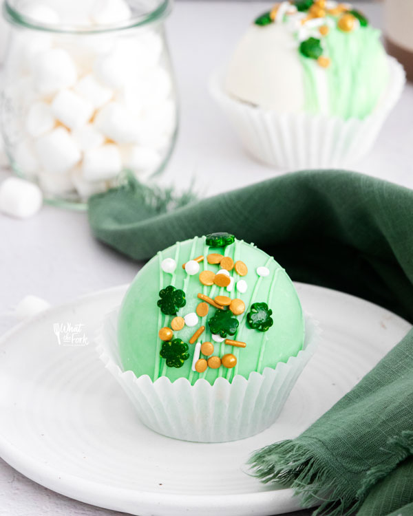 a green St. Patrick's Day Hot Cocoa Bombs in a white paper liner on a white plate