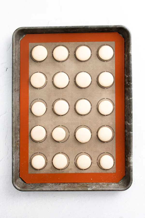 Baileys Irish Cream Macaron shells on a half sheet baking pan lined with a Silpat Macaron Mat