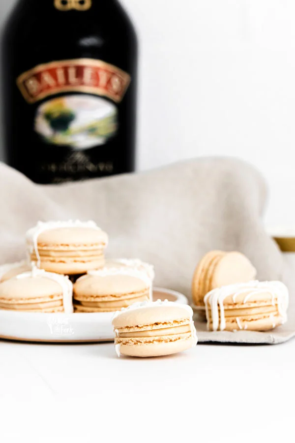 finished Baileys Irish Cream Macaron Recipe on a white plate and surface with a bottle of Baileys in the background