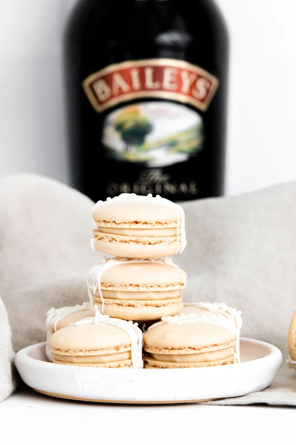 a stack of Baileys Irish Cream Macaron Recipe on a white plate with a bottle of Baileys in the background