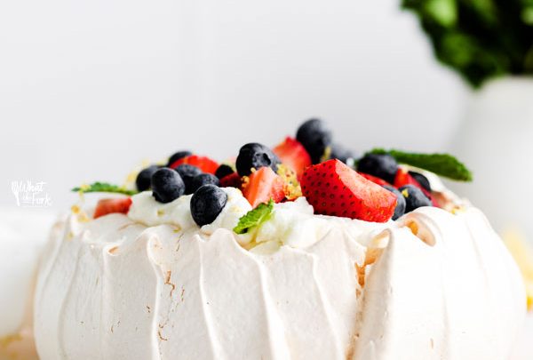 a finished classic pavlova recipe served on a white cake plate and topped with fresh berries and mint