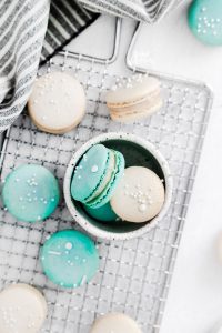 overhead shot of white and blue macarons on a wire rack and in a small white bowl