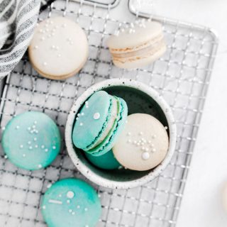 overhead shot of white and blue macarons on a wire rack and in a small white bowl