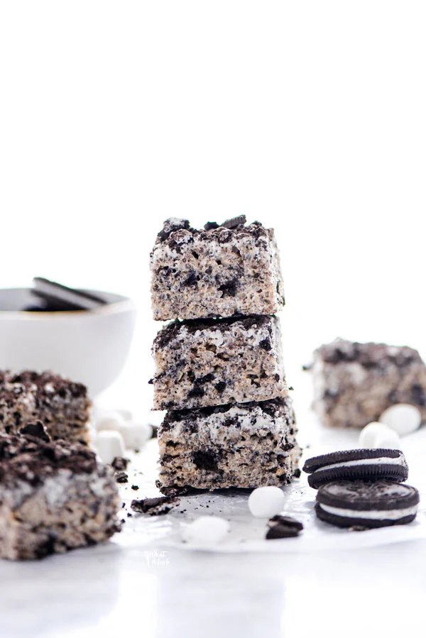 Gluten Free Cookies and Cream Rice Krispie Treats stacked on a white surface with mini marshmallows and gluten free oreos around