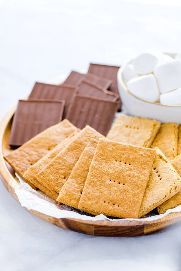 gluten free graham crackers on a round wood tray with chocolate bars and marshmallows