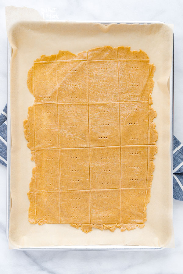 gluten free graham cracker dough on a parchment lined-baking sheet ready to be baked