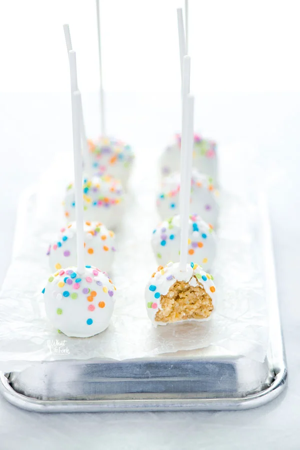 confetti cake pops on a serving tray, one with a bite taken out