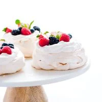 baked and assembled mini pavlovas on a white marble and wood cake stand