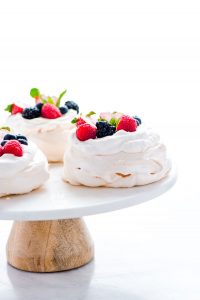 baked and assembled mini pavlovas on a white marble and wood cake stand