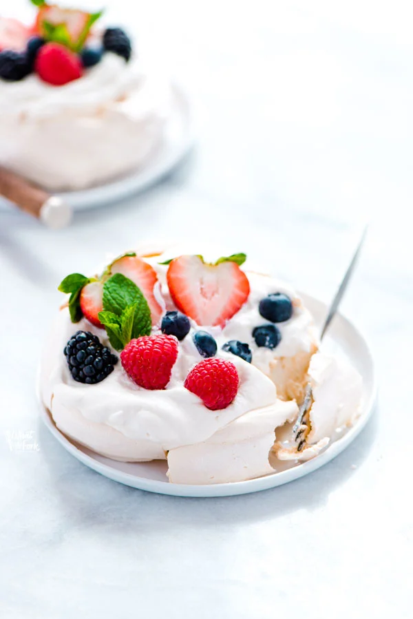 an individual mini pavlova on a small white plate with a fork bite taken out