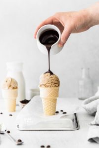 No Churn Coffee Ice Cream in an ice cream cone with chocolate sauce being poured on top