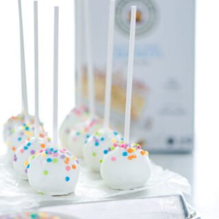 finished Gluten Free Confetti Cake Pop Recipe on an overturned sheet pan lined with wax paper with a box of King Arthur Gluten Free Confetti Cake Mix in the background