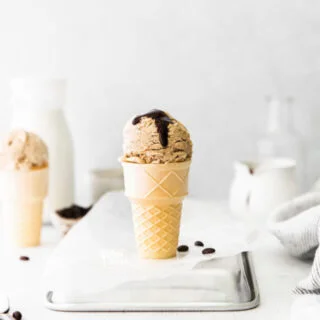 a scoop of No Churn Coffee Ice Cream Recipe served in a cake cone topped with a drizzle of chocolate sauce