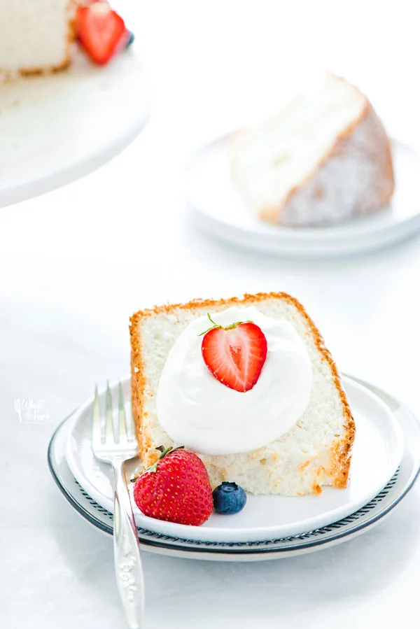 a piece of gluten free angel food cake on a white plate garnished with whipped cream and fresh berries