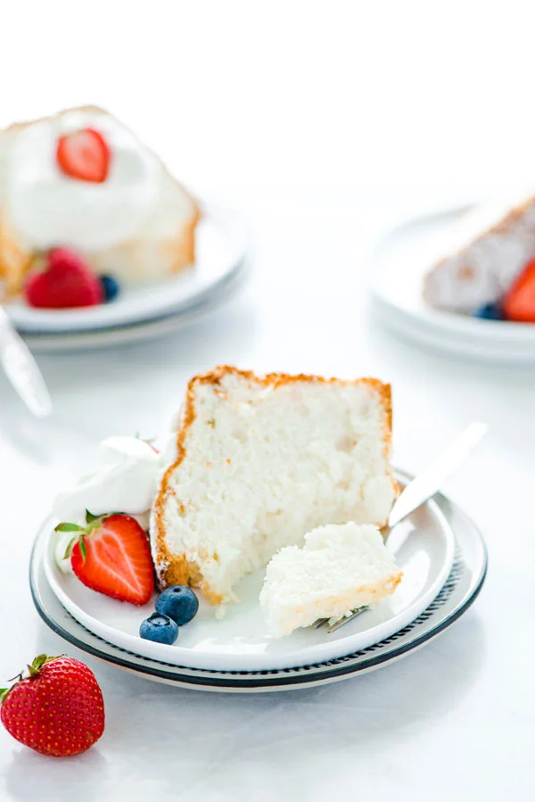 a slice of gluten free angel food cake on a plate garnished with fresh berries and a fork removing a bite