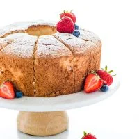 Gluten Free Angel Food Cake on a white and wood cake stand garnished with fresh berries and dusted with powdered sugar