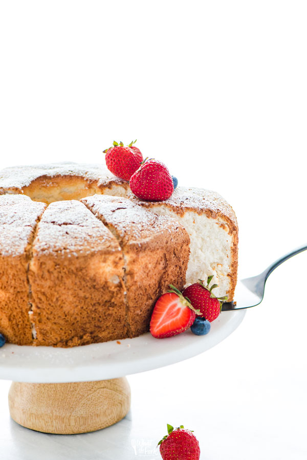 A slice of guten free angel food cake being removed from a cake stand with a black cake server